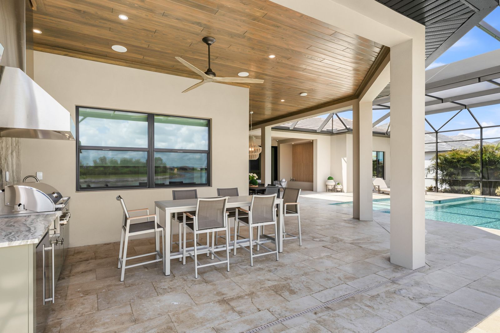 Screened pool lanai with a stained tongue-and-groove wood ceiling, recessed lights and a fan above an outdoor kitchen and seating area